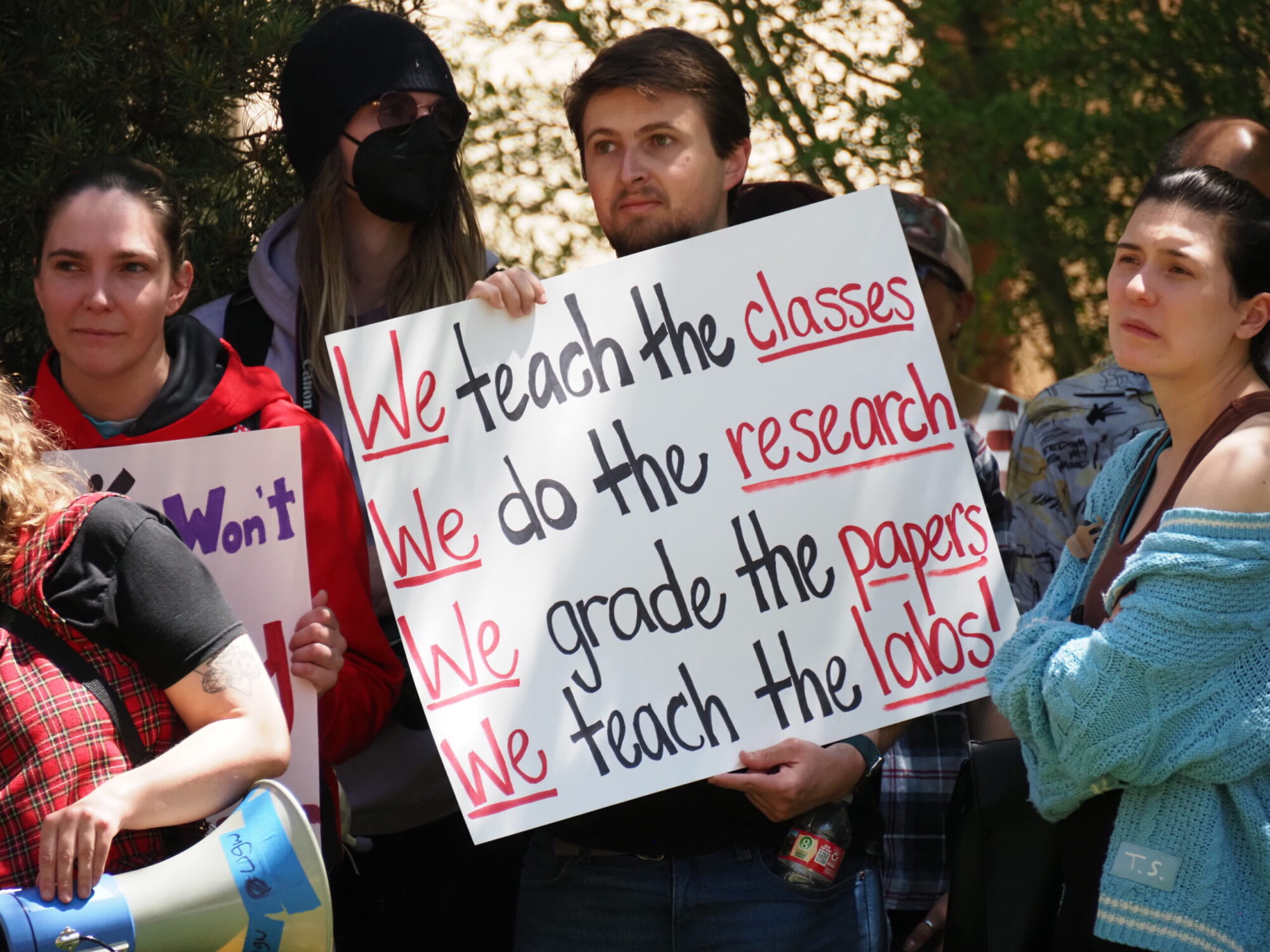 UGW Steward holding a sign that reads "We teach the classes, we do the research, we grade the papers, we teach the labs!"